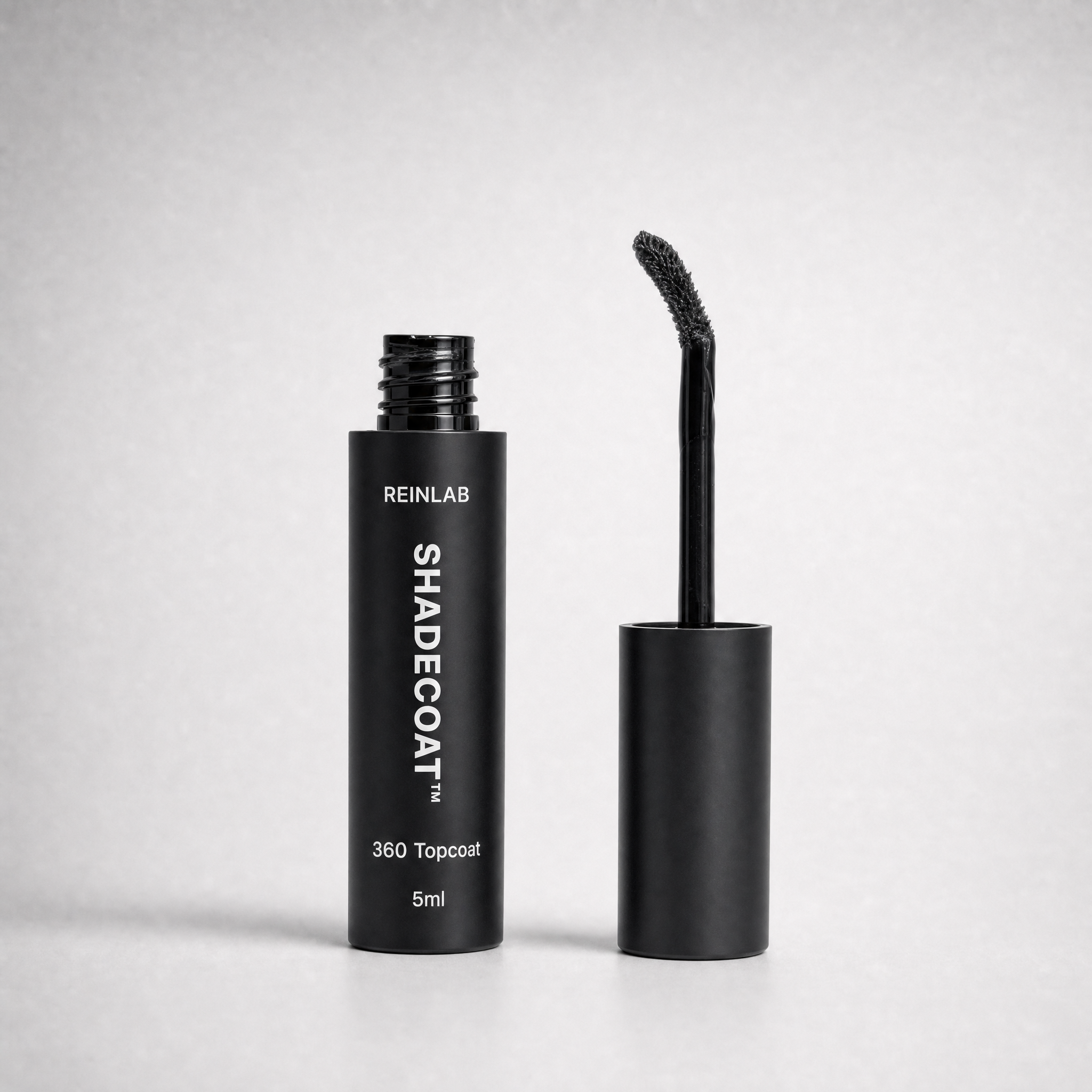 Black REINLAB SHADECOAT 360 Topcoat 5ml cosmetic tube shown next to its applicator wand on a light gray background.